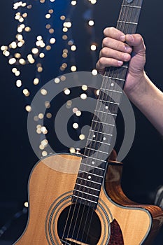 Acoustic guitar in the hands of a guitarist on a dark background with bokeh.