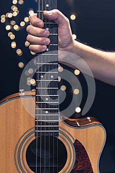 Acoustic guitar in the hands of a guitarist on a dark background with bokeh.