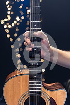 Acoustic guitar in the hands of a guitarist on a dark background with bokeh.