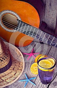 Acoustic guitar hat starfish and glass of tasty fresh lemonade with lemons on vintage wood