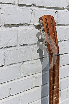 Acoustic guitar headstock against white brick wall