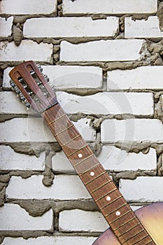 Acoustic guitar headstock against white brick wall