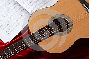 Acoustic guitar and music notes on red fabric, close view of objects