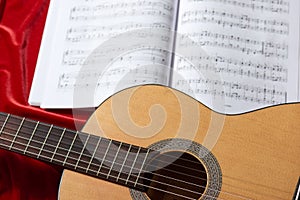 Acoustic guitar and music notes on red fabric, close view of objects