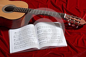 Acoustic guitar and music notes on red velvet fabric, close view of objects