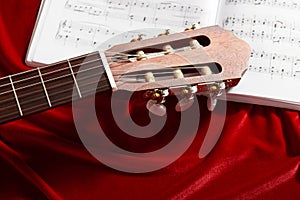 Acoustic guitar and music notes on red velvet fabric, close view of objects