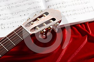 Acoustic guitar and music notes on red velvet fabric, close view of objects
