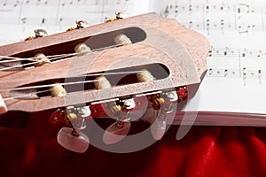 Acoustic guitar and music notes on red velvet fabric, close view of objects