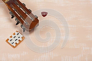 Acoustic guitar neck, tuning fork and pick. Against a background painted in white and beige