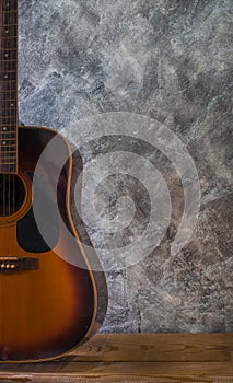 Acoustic guitar resting against on wooden table a blank cement wall