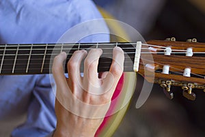 Acoustic guitar's fretboard and young male's hand