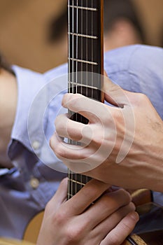 Acoustic guitar's fretboard and young male's hands