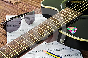 Acoustic guitar, sunglasses and sheet musical notes on the table