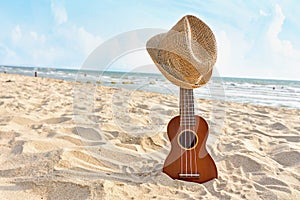 Acoustic ukulele standing in the sandy beach with hat