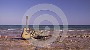 Acoustic western guitar on beach or shore with background sea or ocean. Only guitar ashore ocean with waves on stones