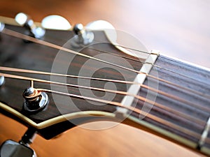 Acoustic wood guitar close up on wooden background with fretboard, strings, and tuners for music blogs, website banners.