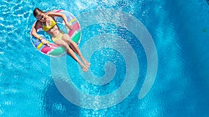 Acrive girl in swimming pool aerial top view from above, kid swims on inflatable ring donut , child has fun in blue water