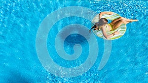 Acrive girl in swimming pool aerial top view from above, kid swims on inflatable ring donut , child has fun in blue water