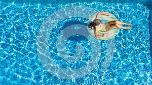 Acrive girl in swimming pool aerial top view from above, kid swims on inflatable ring donut , child has fun in blue water