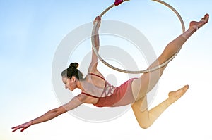 Acrobat athletic, young graceful gymnast performing aerial exercise in the air ring outdoors on sky background at sunset. flexible