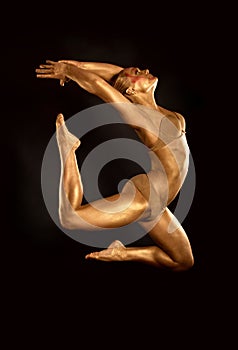 Acrobat dancer toned in gold jumping over black background