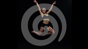 Acrobat girl jumps bending the knees. Slow motion. Black background