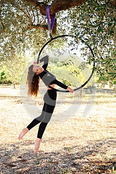 Acrobat making a pose on aerial circle among olive trees in summer