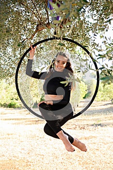 Acrobat making a pose on aerial hoop or circle among olive trees in summer