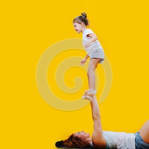 Acrobatic girl standing on mom`s hands, happy and exhilarated over yellow