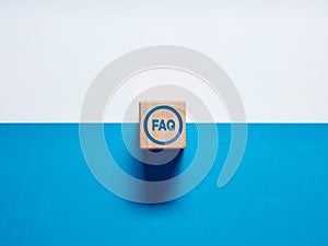 The acronym FAQ Frequently Asked Questions on wooden cube push button on blue and white background