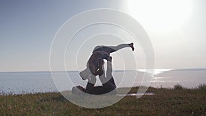 Acroyoga, two sporty people practicing yoga in pair on nature sunset background, young couple doing stretching exercise