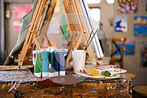 Acrylic paints tubes, pallets and wooden easels on table in art class or artist studio workplace