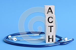 ACTH word written on wooden blocks and stethoscope on light blue background