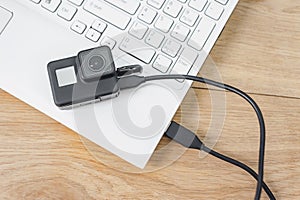 Action-camera connected to a white laptop, against the background of a wooden table