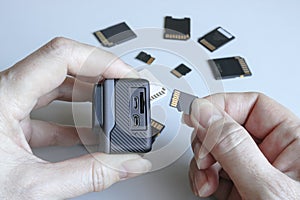 Action camera and microSD memory card in hands on the back of other SD memory cards. Background from gadgets and digital devices