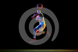 Action photo of young athlete man, basketball player doing pass against black studio background in mixed neon light.