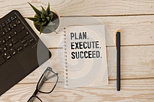 Action Plan Plan, Execute, Succed writing on notebook. Notebook on desk