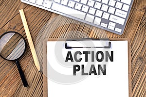 ACTION PLAN text on paper clipboard with magnifier and keyboard on wooden background