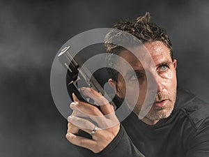 Action portrait of serious and attractive hitman or special agent man holding gun pointing the handgun at cinematic edgy