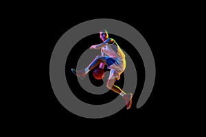 Action shot of basketball player's crossover dribble against black studio background in mixed neon light.