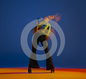 Action. Young girl dancing heels dance in stylish clothes over blue background in neon with mixed lights. Concept of