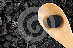 Activated carbon pill medicine in wooden spoon on ground charcoal photo