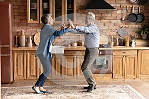 Active aged family couple cooking dancing at modern wooden kitchen