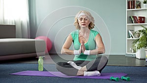 Active aged woman practicing yoga in lotus pose, meditation at home, harmony