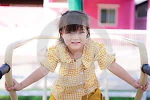 Active Asian child girl is climbing playing and exercising. Adorable girl is wearing a yellow-white checkered dress.