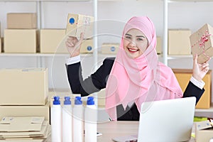 Active asian muslim woman in blue suit sitting and working with computer and showing online package box delivery with happy smilin