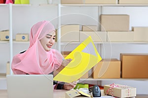 Active asian muslim woman wearing suit sitting and holding folder with computer and online package box delivery. Startup small