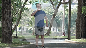 Active athletic young man runner jogging in park. Fit male sport fitness training. Drinking water