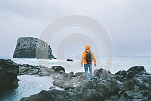 An active backpacker man dressed orange waterproof jacket with backpack enjoying Atlantic ocean bay view on rocky Madeira island