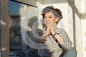 An active, beautiful middle-aged woman with a beautiful smile. Sitting on the windowsill near the window. Reflection in the window